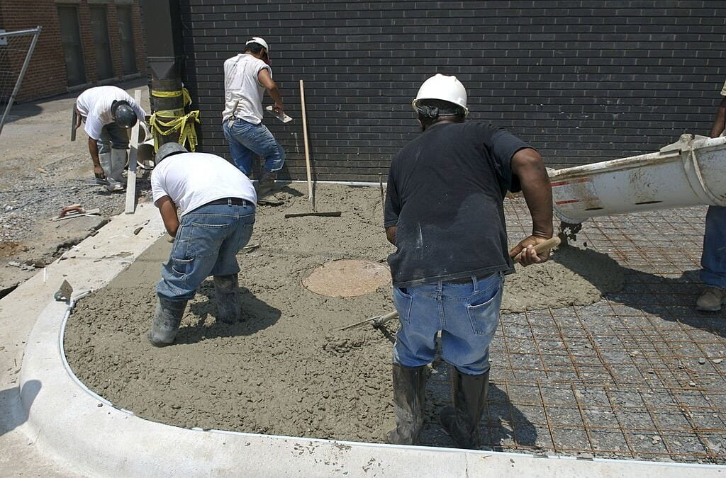 Construction workers pour wet concrete into a mold for a new sidewalk - concrete work