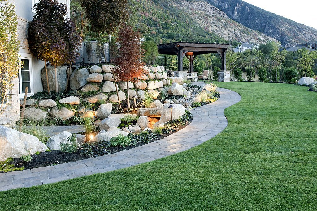 A beautiful landscaped backyard with outdoor lighting with concrete Walkway